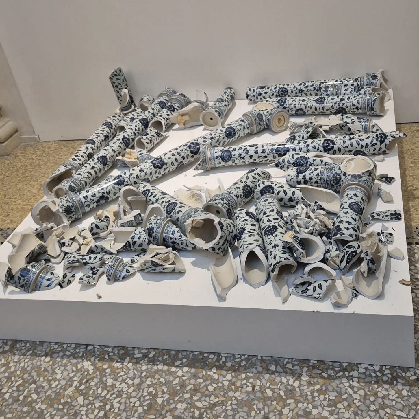 Blue and white pieces of a porcelain sculpture are arranged on a short, white square platform.